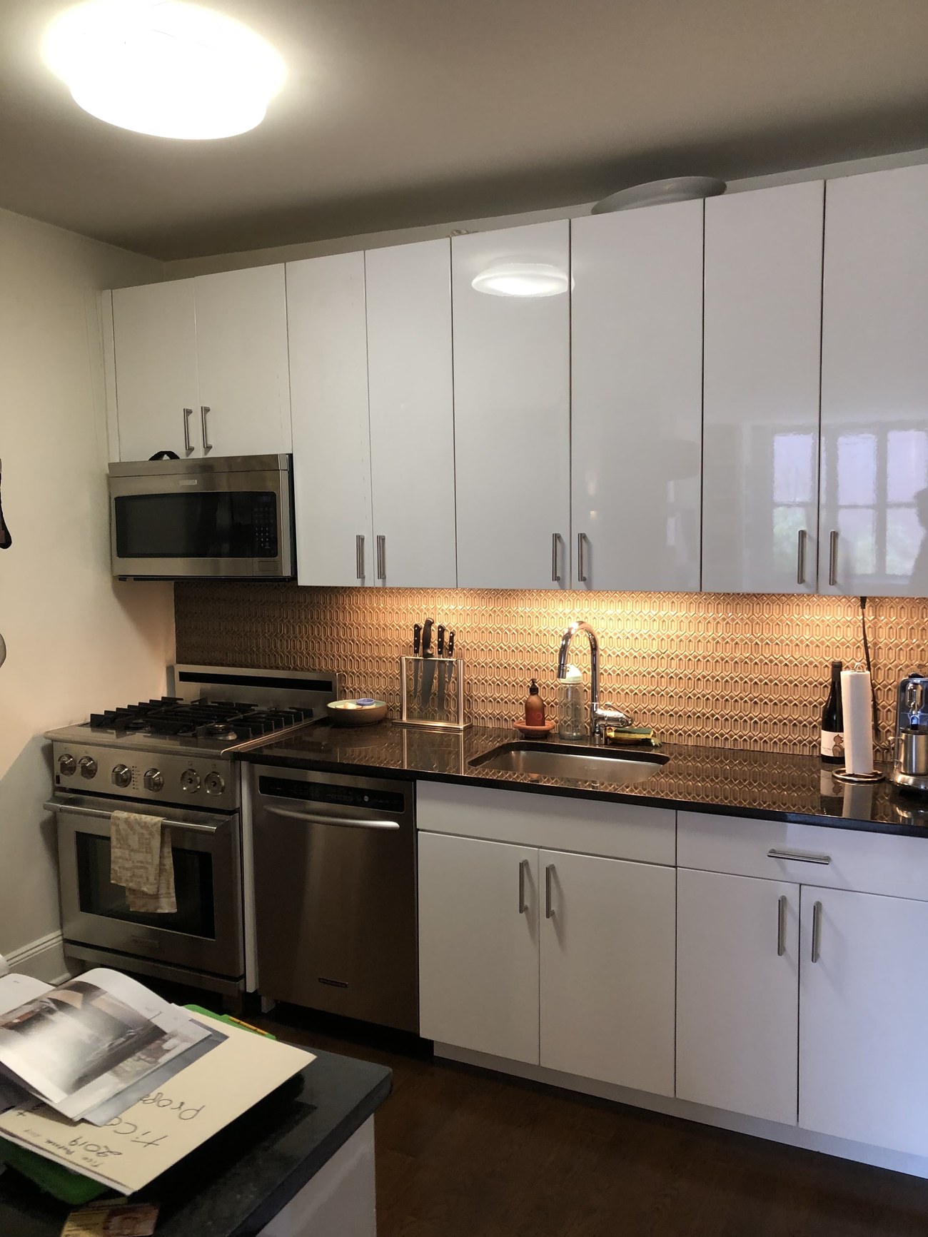 Uptown Manhattan kitchen renovation with high-gloss white cabinetry, copper geometric tile backsplash, and stainless steel appliances — Fuenmayor Solutions LLC
